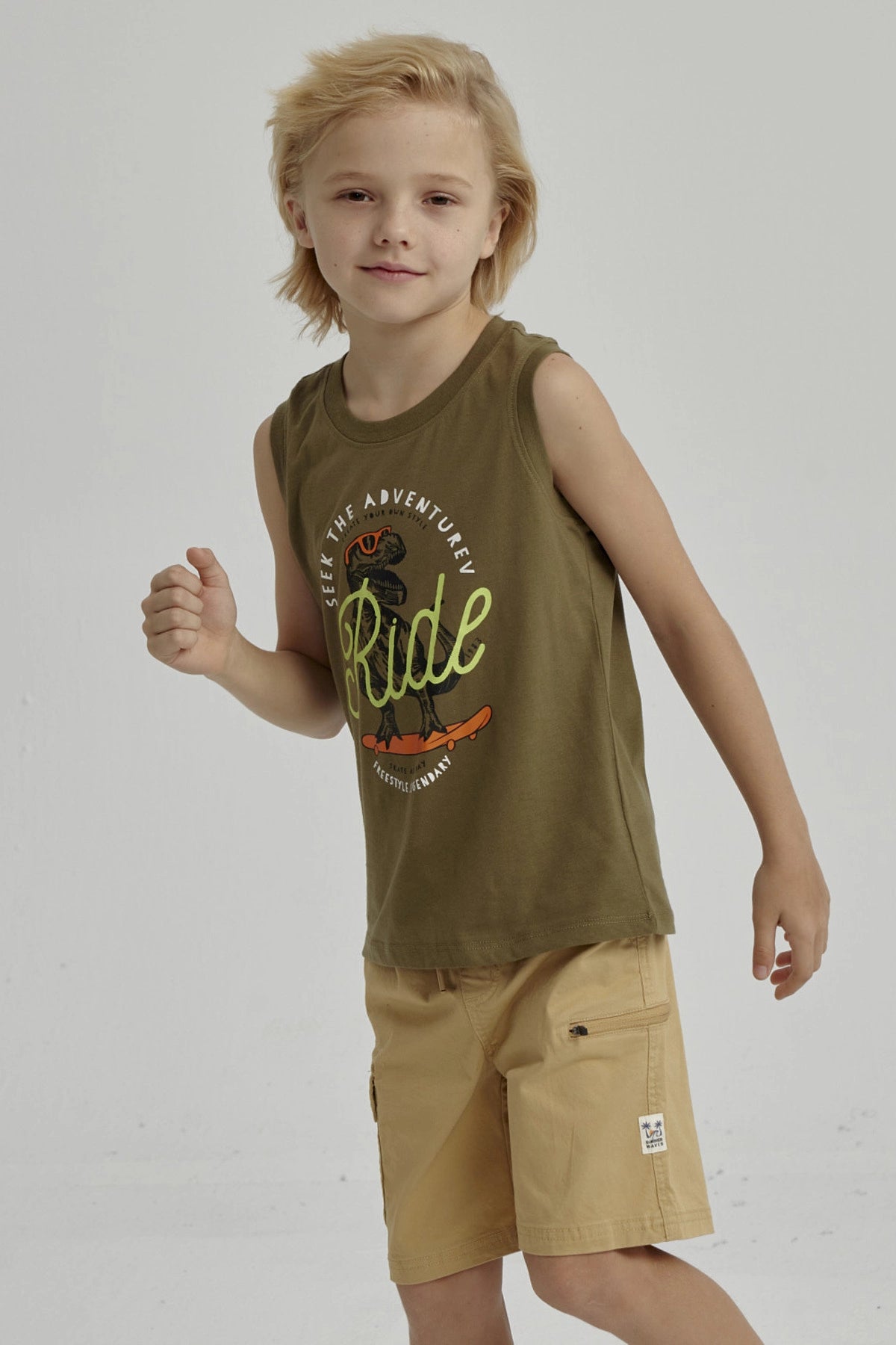 Polera sin mangas verde militar con estampa central de dinosaurio en patineta y texto en estilo urbano