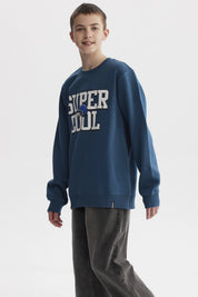 Polerón niño color petróleo con texto SUPER COOL y casco azul al centro en estilo deportivo casual y cómodo