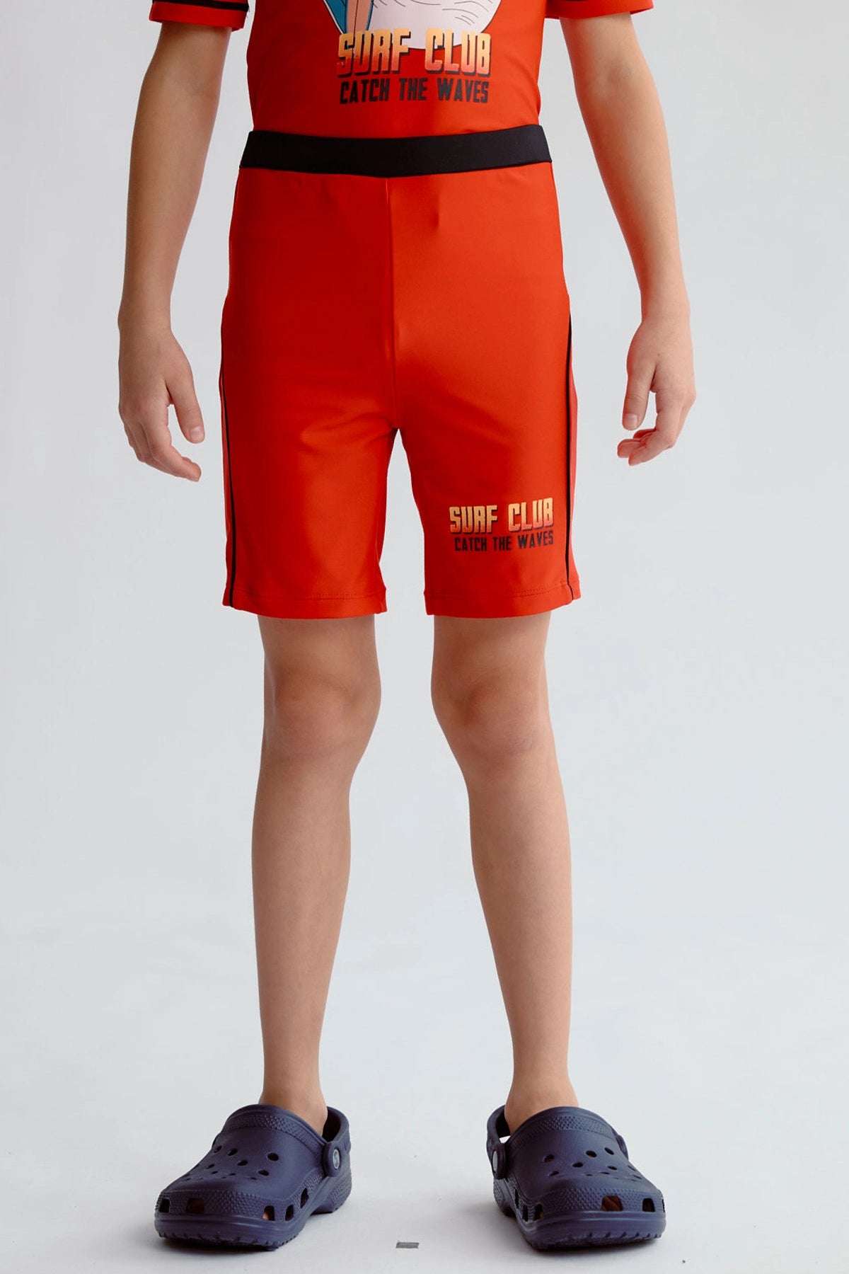 Short de baño niño rojo con cinturilla negra y texto Surf Club en la pierna