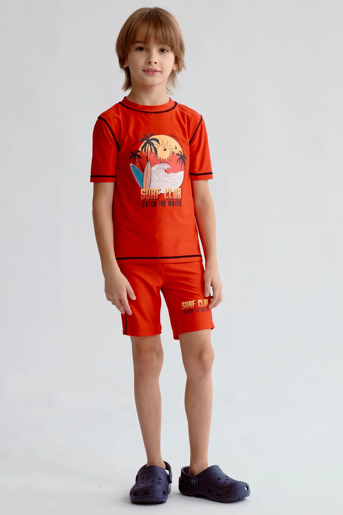 Short de baño niño rojo con cinturilla negra y texto Surf Club en la pierna