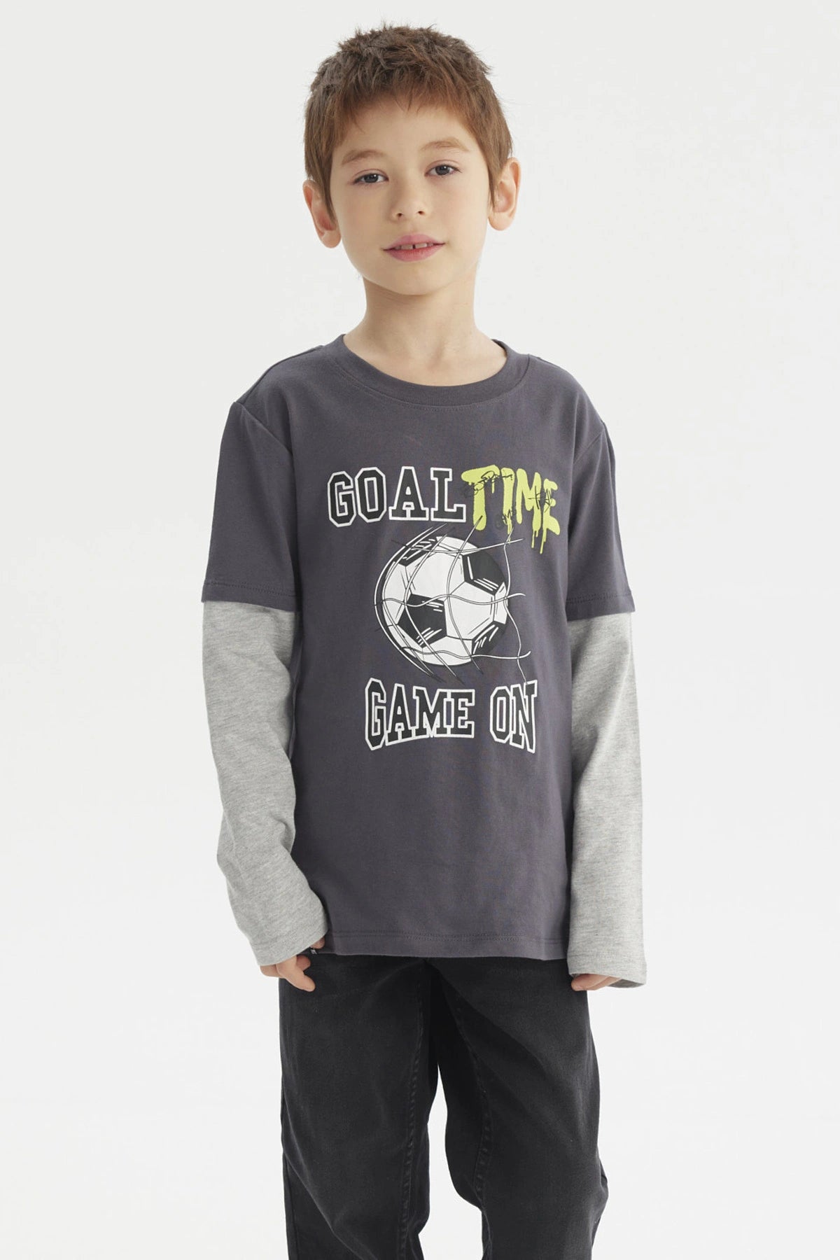 Polera de niño color marengo con estampado delantero de balón de fútbol y texto Goal Time Game On estilo deportivo casual