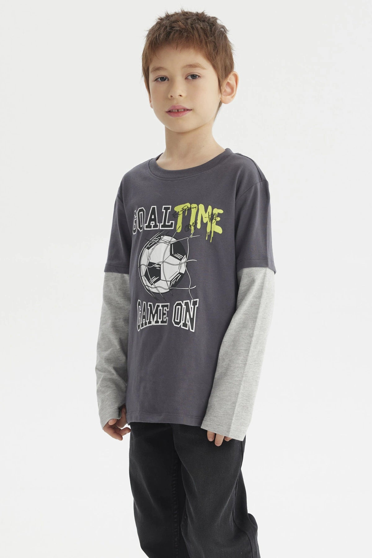 Polera de niño color marengo con estampado delantero de balón de fútbol y texto Goal Time Game On estilo deportivo casual