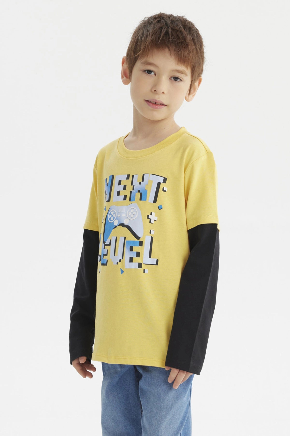 Polera amarilla para niño con mangas largas negras y estampado de control de videojuego y texto Next Level en el frente