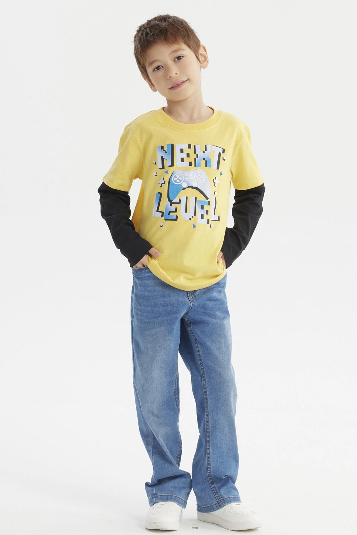 Polera amarilla para niño con mangas largas negras y estampado de control de videojuego y texto Next Level en el frente