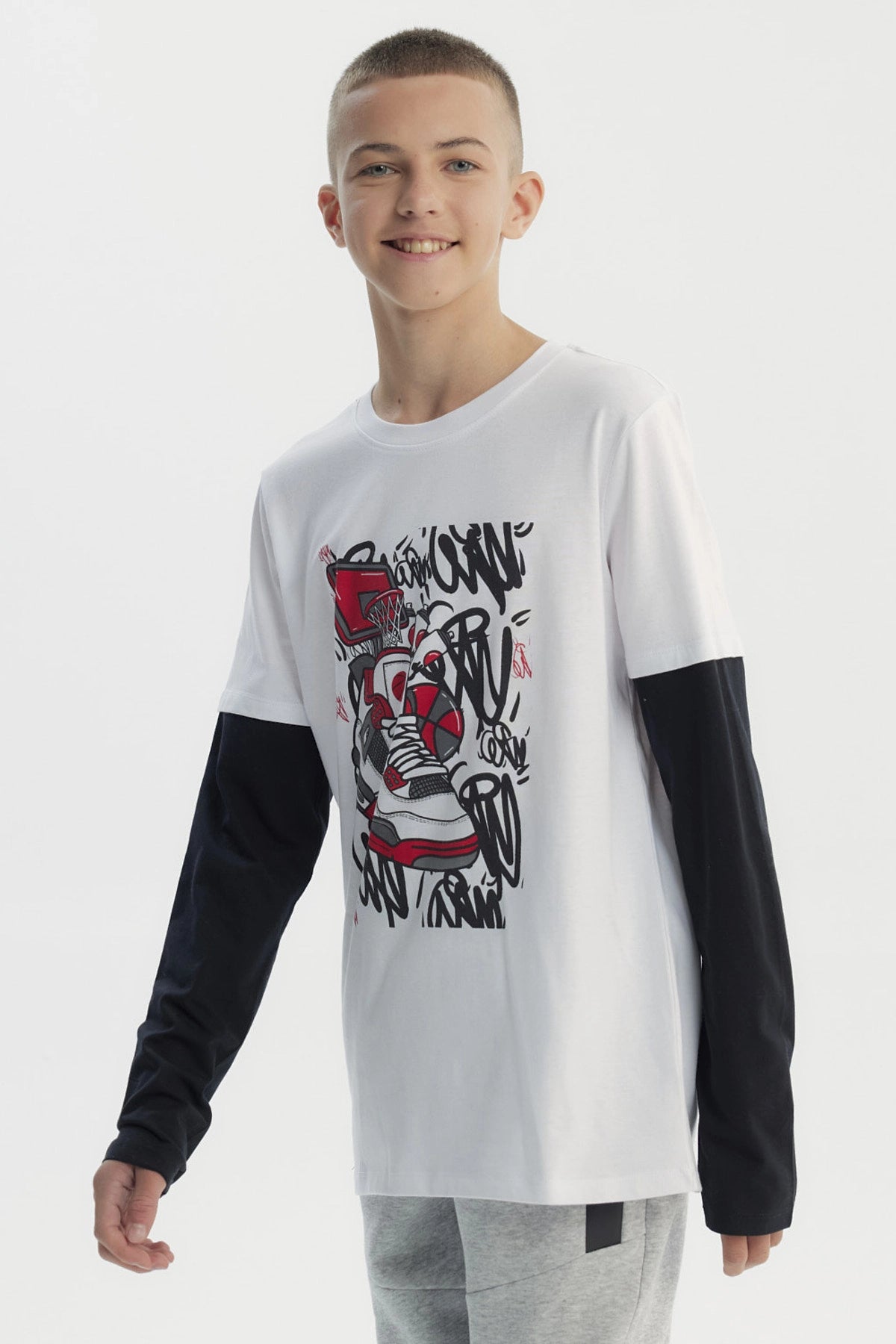 Polera niño blanca con mangas largas negras y estampa de zapatilla roja y negra en el centro con fondo de grafitis