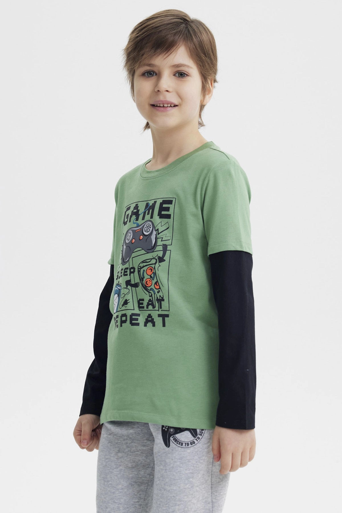 Polera niño verde claro con estampa central de videojuego con control consola pizza y texto GAME SLEEP EAT REPEAT