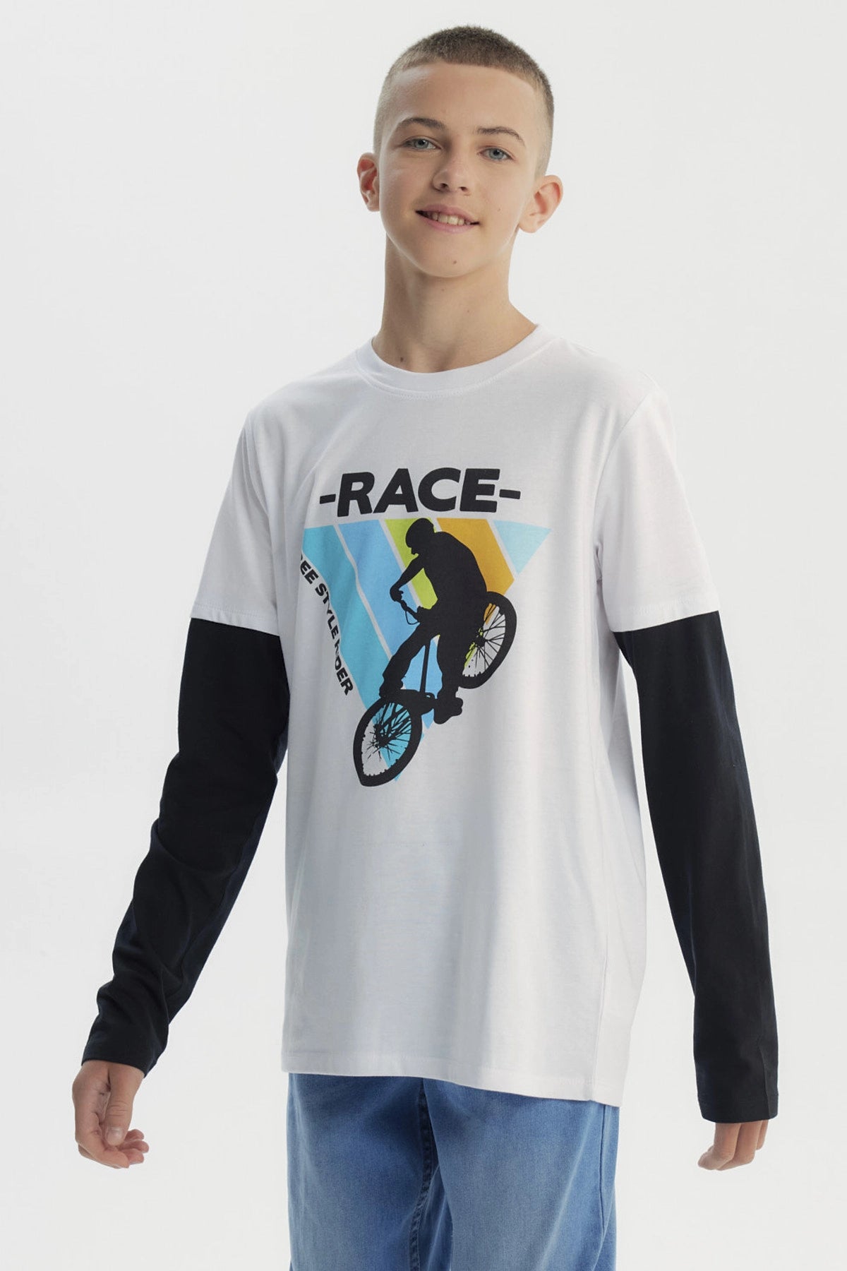 Polera niño blanca con mangas largas negras y estampa de ciclista freestyle en el centro sobre fondo de franjas azules y amarillas
