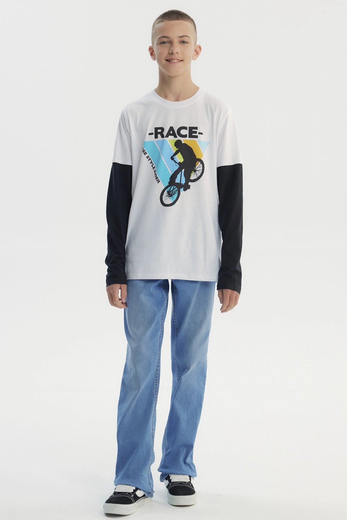 Polera niño blanca con mangas largas negras y estampa de ciclista freestyle en el centro sobre fondo de franjas azules y amarillas