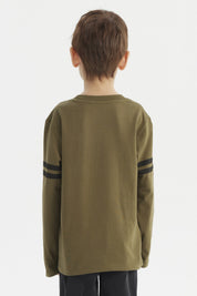 Polera de niño verde militar con dinosaurio azul y texto Roaar Explore More al frente estilo gráfico divertido