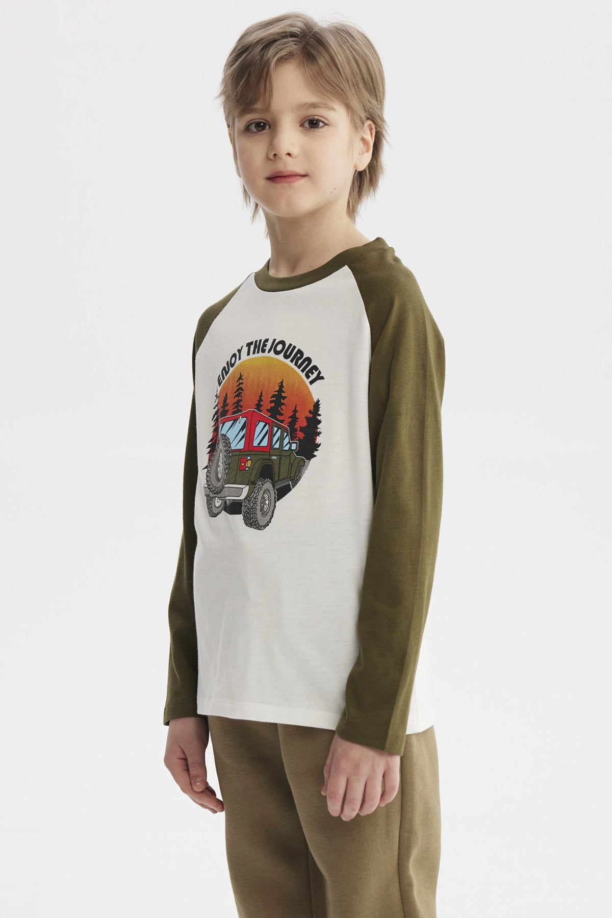 Polera cruda de niño con mangas largas verdes y estampado central de un jeep en un bosque al atardecer con texto Enjoy the Journey
