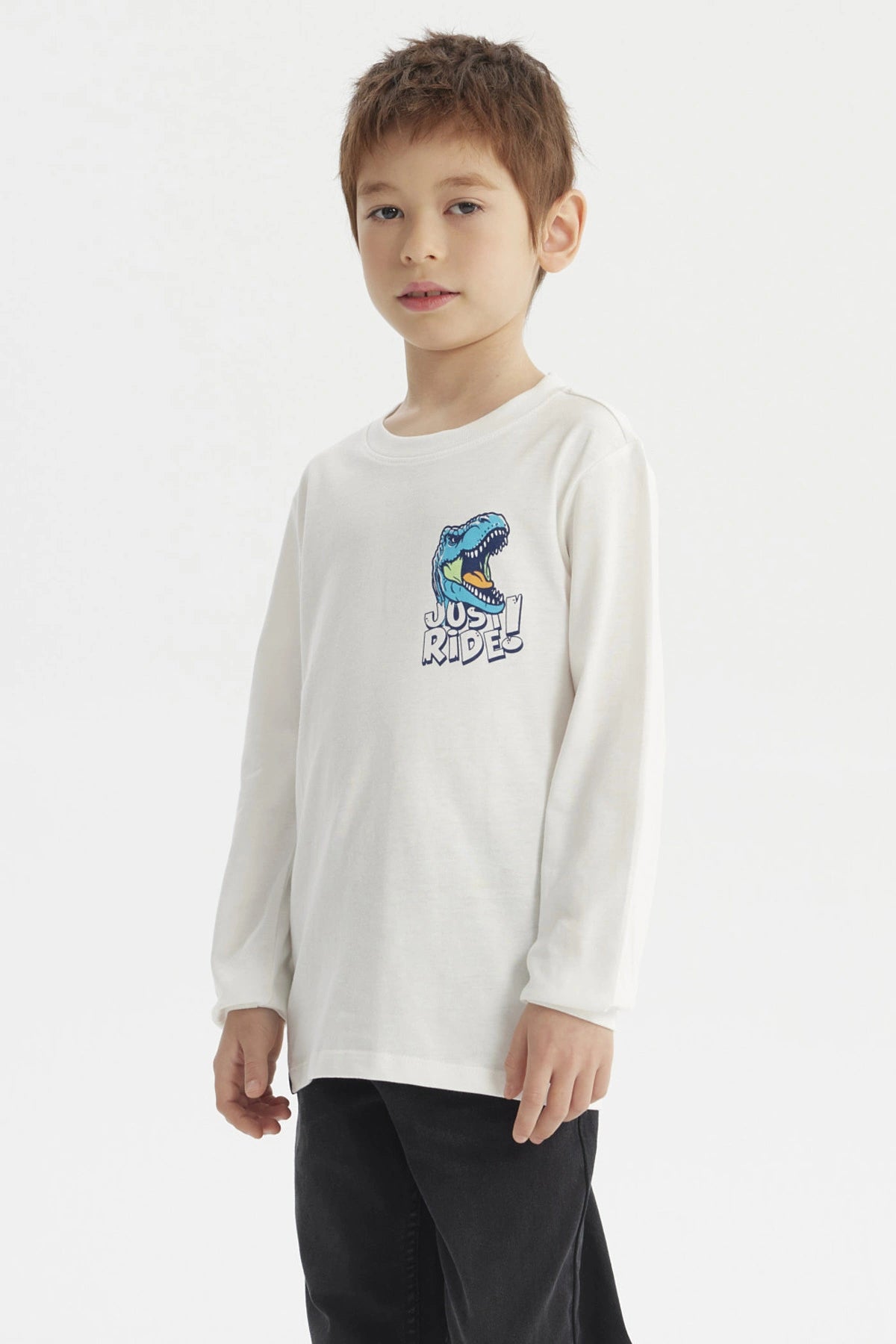Polera crudo de niño con estampa de dinosaurio azul y texto Just Ride en el pecho estilo casual y gráfico