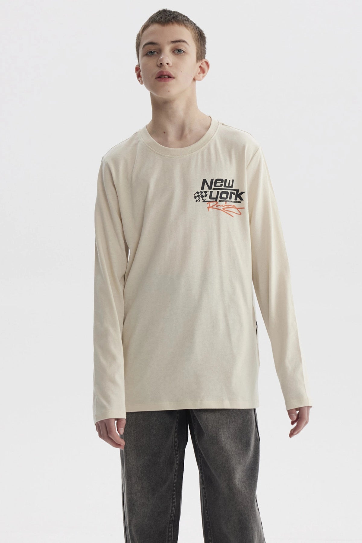 Polera de niño color crudo con estampado de texto 'New York' y bandera de cuadros en el pecho estilo urbano moderno
