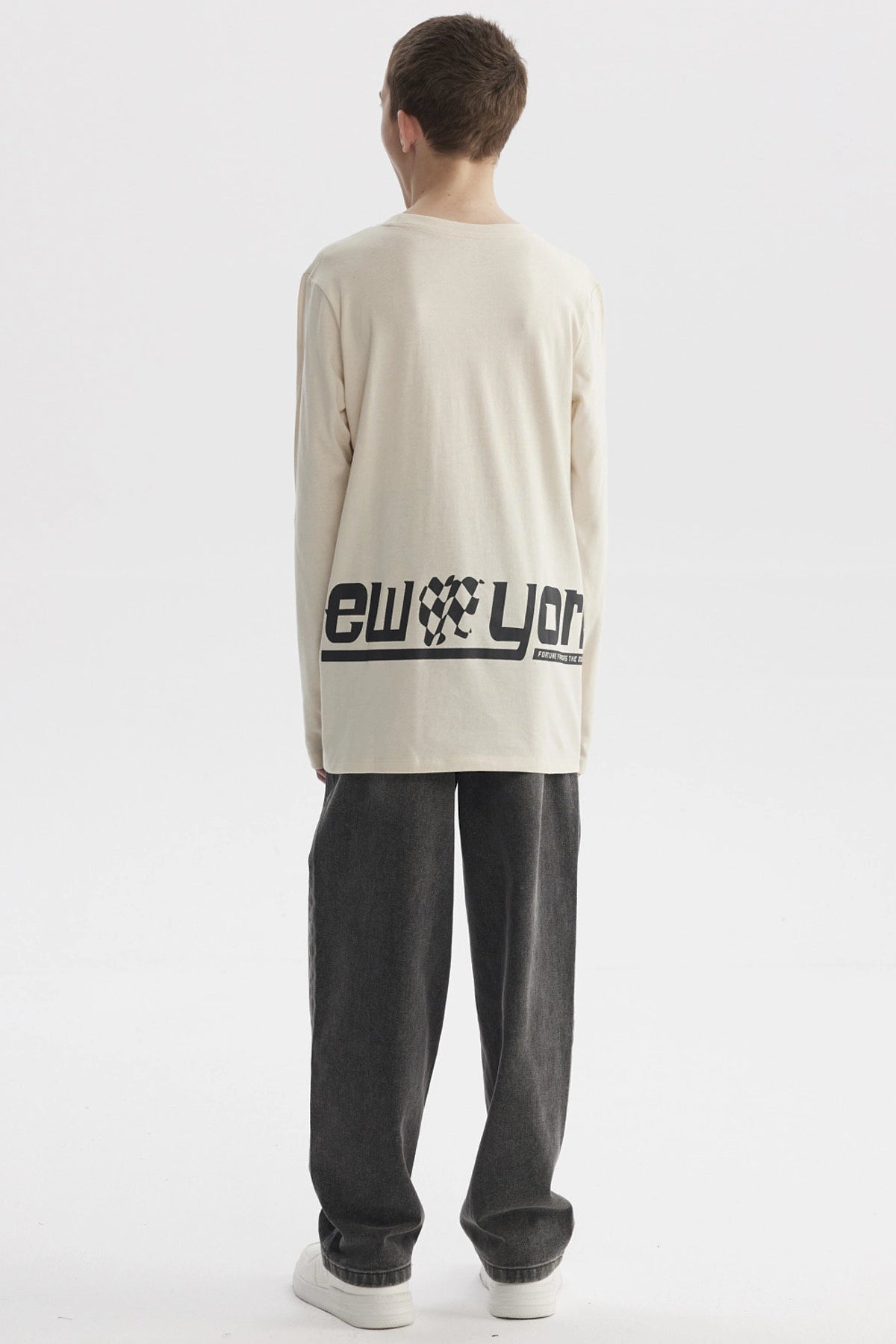 Polera de niño color crudo con estampado de texto 'New York' y bandera de cuadros en el pecho estilo urbano moderno