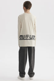 Polera de niño color crudo con estampado de texto 'New York' y bandera de cuadros en el pecho estilo urbano moderno