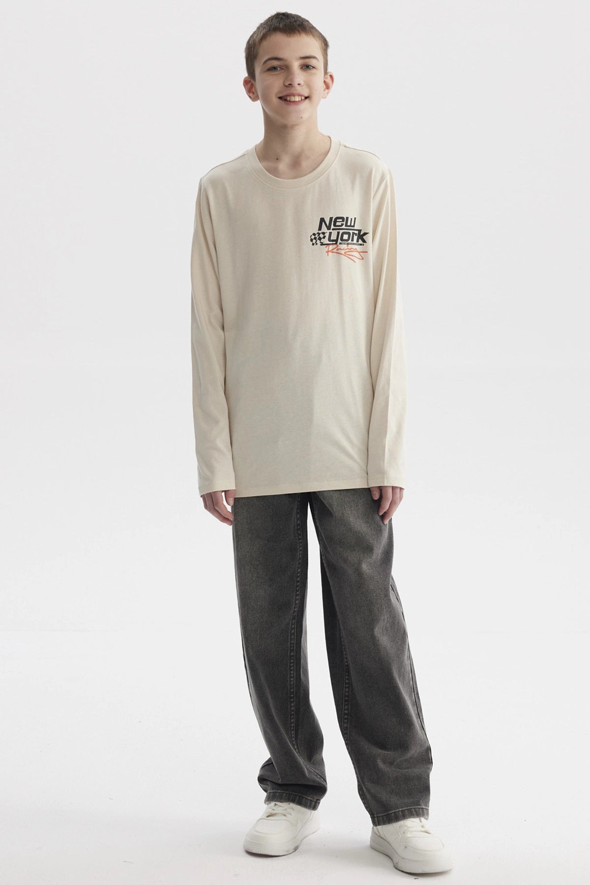 Polera de niño color crudo con estampado de texto 'New York' y bandera de cuadros en el pecho estilo urbano moderno