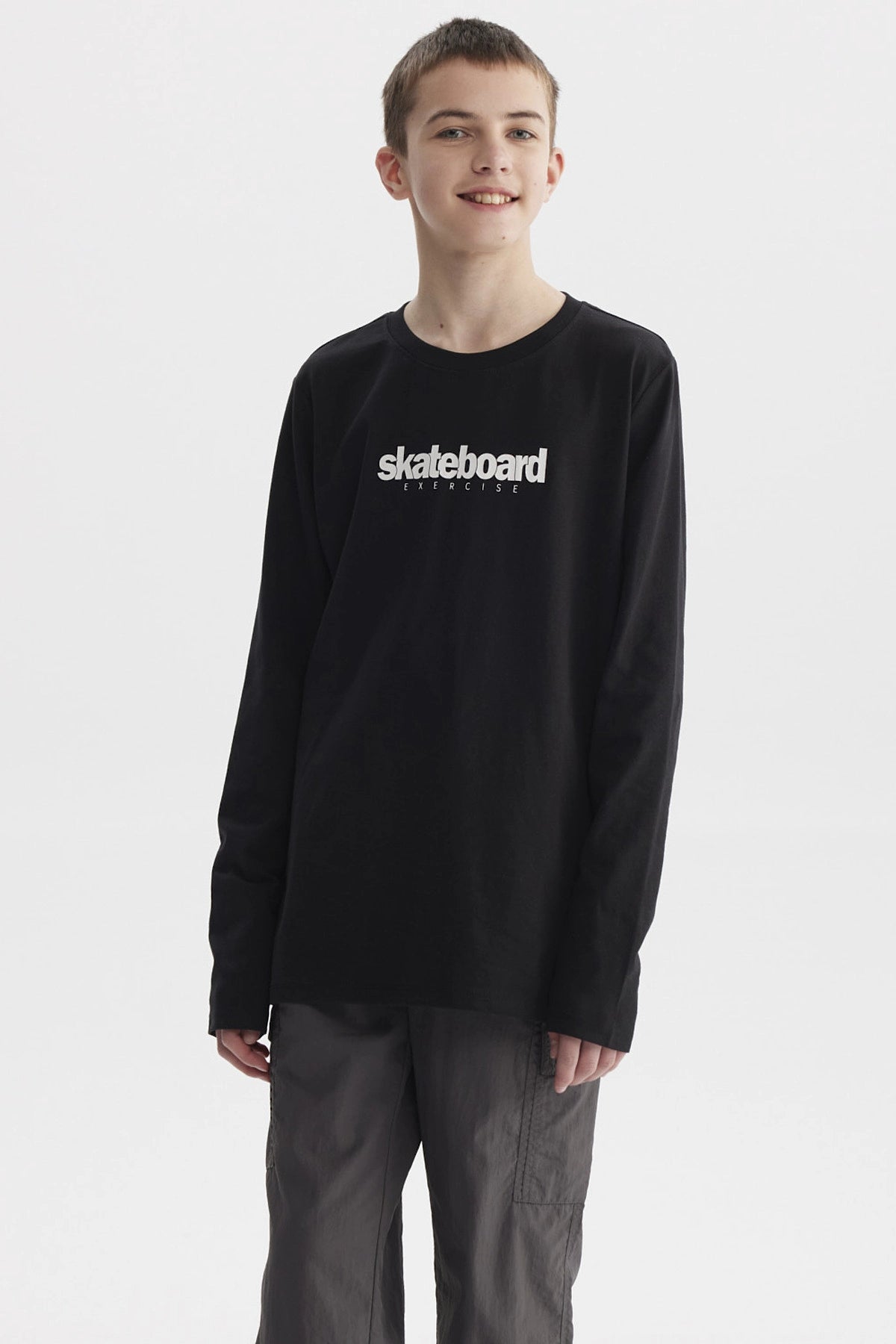 Polera negra de niño con texto blanco skateboard exercise en el pecho estilo casual urbano y manga larga lisa