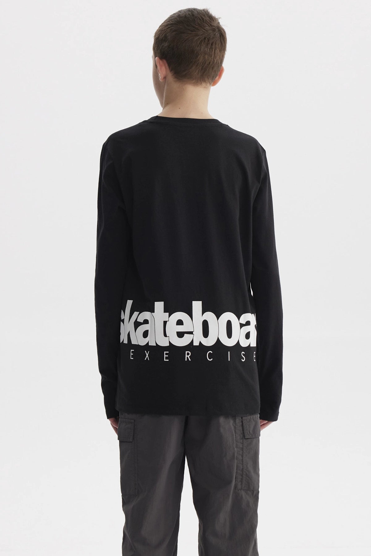 Polera negra de niño con texto blanco skateboard exercise en el pecho estilo casual urbano y manga larga lisa