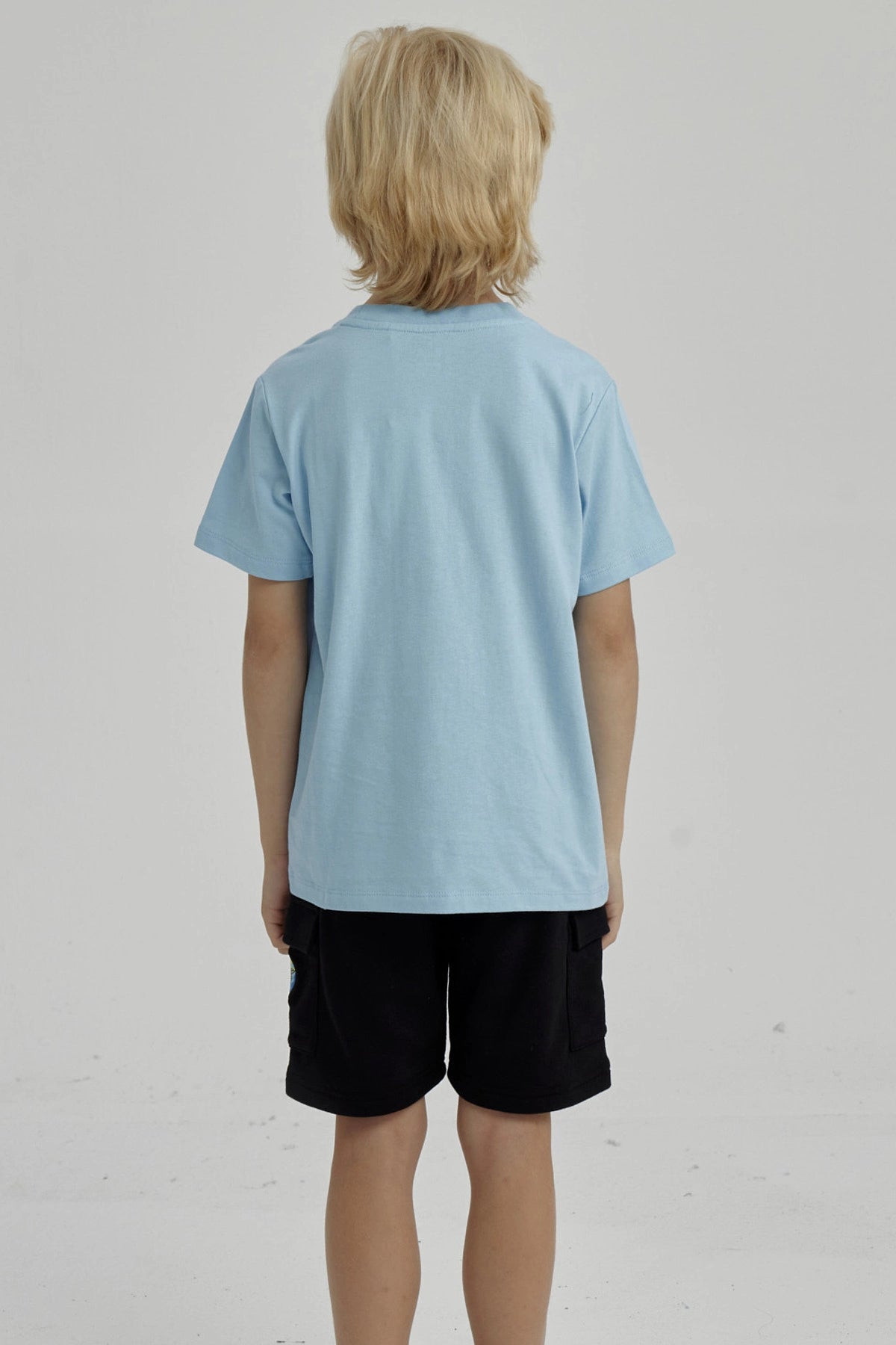 Polera celeste de niño con estampado frontal de surf club con tabla de surf ola y palmera diseño gráfico pequeño