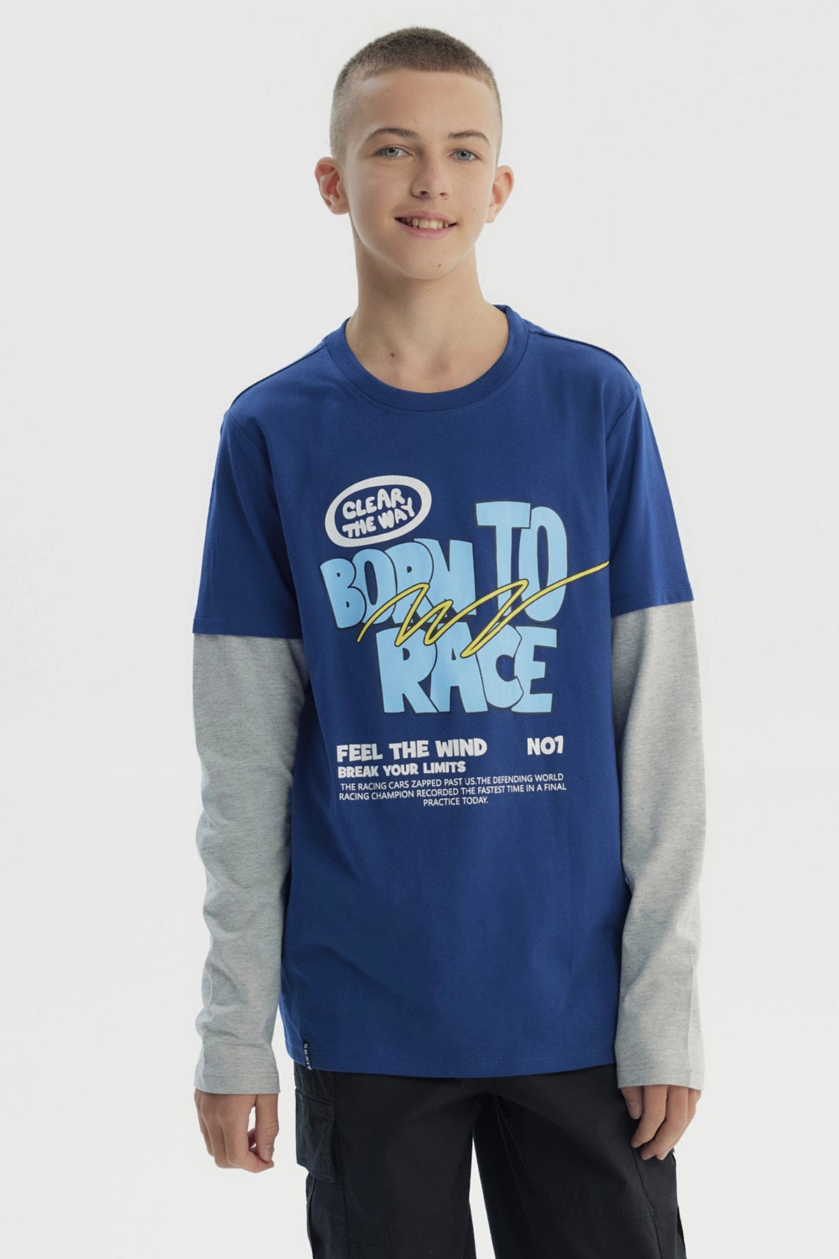 Polera niño azul con estampado frontal de letras en estilo gráfico grande y texto BORN TO RACE sobre fondo liso