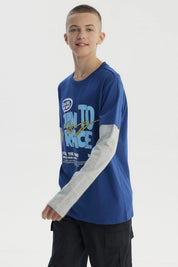 Polera niño azul con estampado frontal de letras en estilo gráfico grande y texto BORN TO RACE sobre fondo liso
