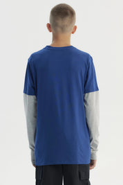 Polera niño azul con estampado frontal de letras en estilo gráfico grande y texto BORN TO RACE sobre fondo liso