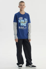 Polera niño azul con estampado frontal de letras en estilo gráfico grande y texto BORN TO RACE sobre fondo liso