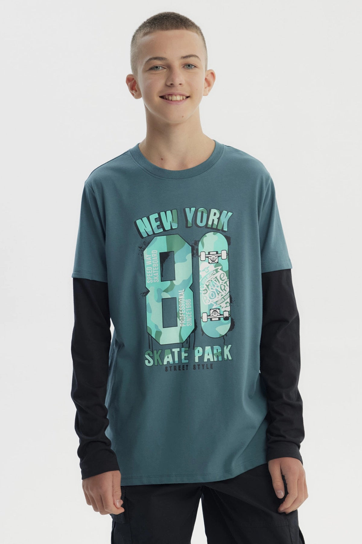 Polera niño verde oscuro con estampado central de texto New York 80 Skate Park y patinetas en estilo urbano graffiti