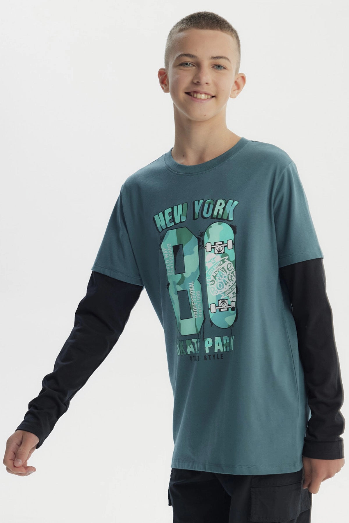 Polera niño verde oscuro con estampado central de texto New York 80 Skate Park y patinetas en estilo urbano graffiti