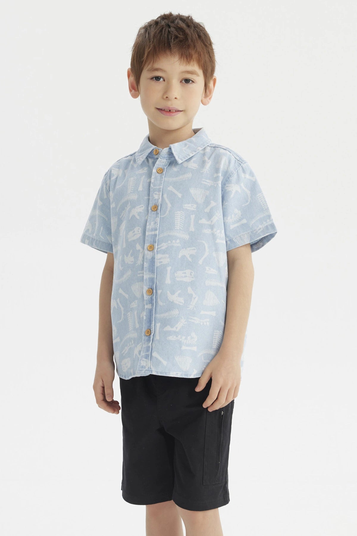 Camisa de niño celeste con estampado de dinosaurios blancos en estilo gráfico pequeño y disperso por toda la prenda