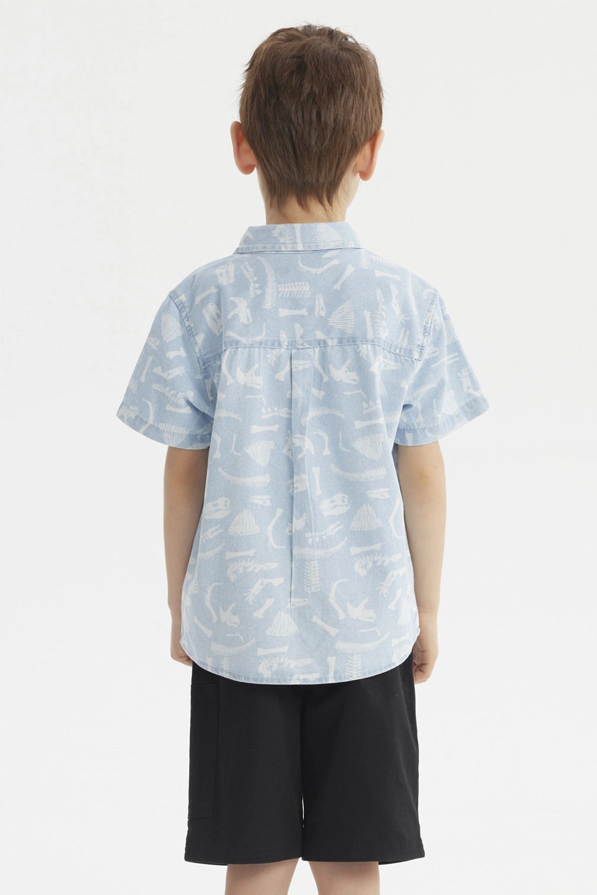Camisa de niño celeste con estampado de dinosaurios blancos en estilo gráfico pequeño y disperso por toda la prenda