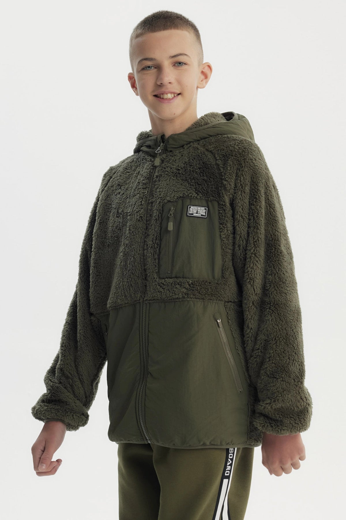 Polar para niño verde militar con capucha cierre completo y bolsillo frontal con parche gráfico estilo urbano