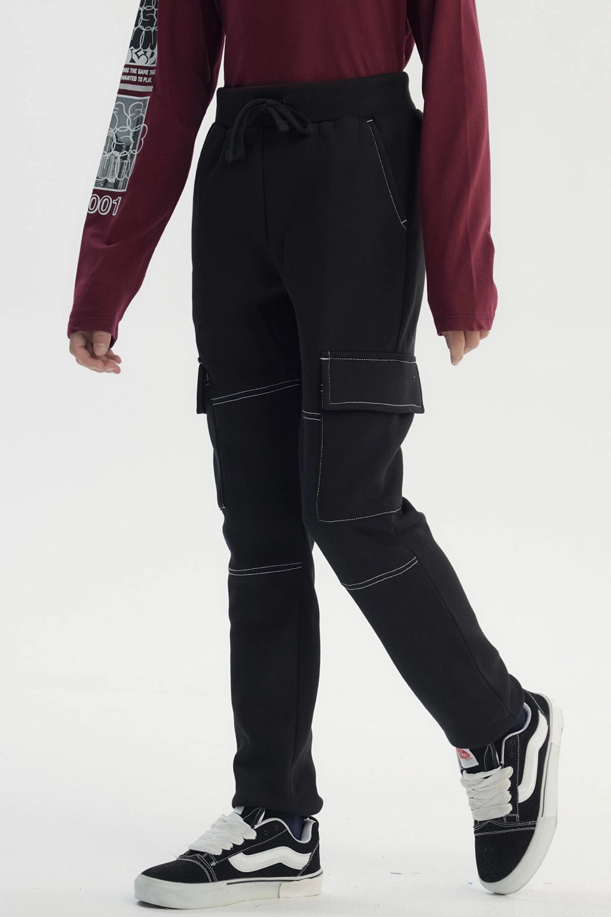Pantalón buzo pitillo negro para niño con bolsillos laterales grandes y costuras blancas visibles estilo casual