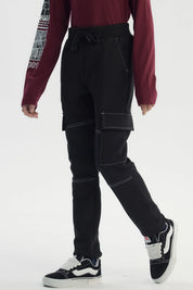 Pantalón buzo pitillo negro para niño con bolsillos laterales grandes y costuras blancas visibles estilo casual