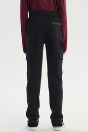 Pantalón buzo pitillo negro para niño con bolsillos laterales grandes y costuras blancas visibles estilo casual