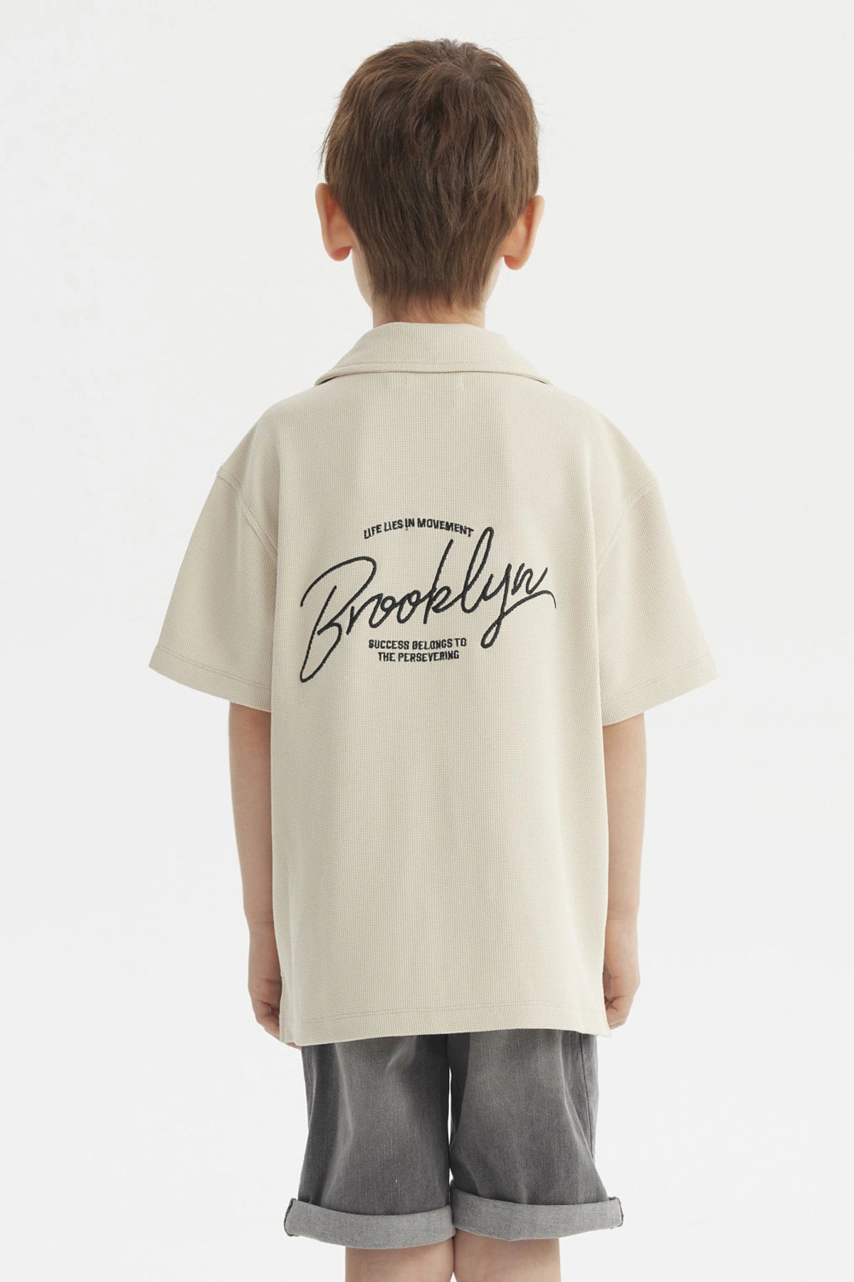 Camisa niño color crudo con cuello abierto y texto Brooklyn en el pecho estilo casual sin estampa adicional