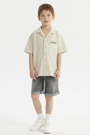 Camisa niño color crudo con cuello abierto y texto Brooklyn en el pecho estilo casual sin estampa adicional