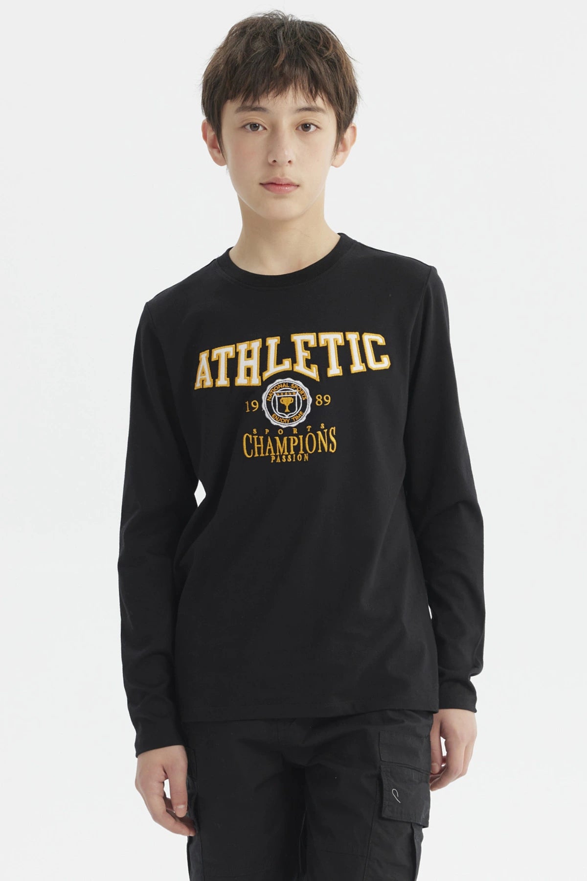 Polera negra de niño con estampado bordado estilo college en el pecho que dice ATHLETIC y detalles en amarillo