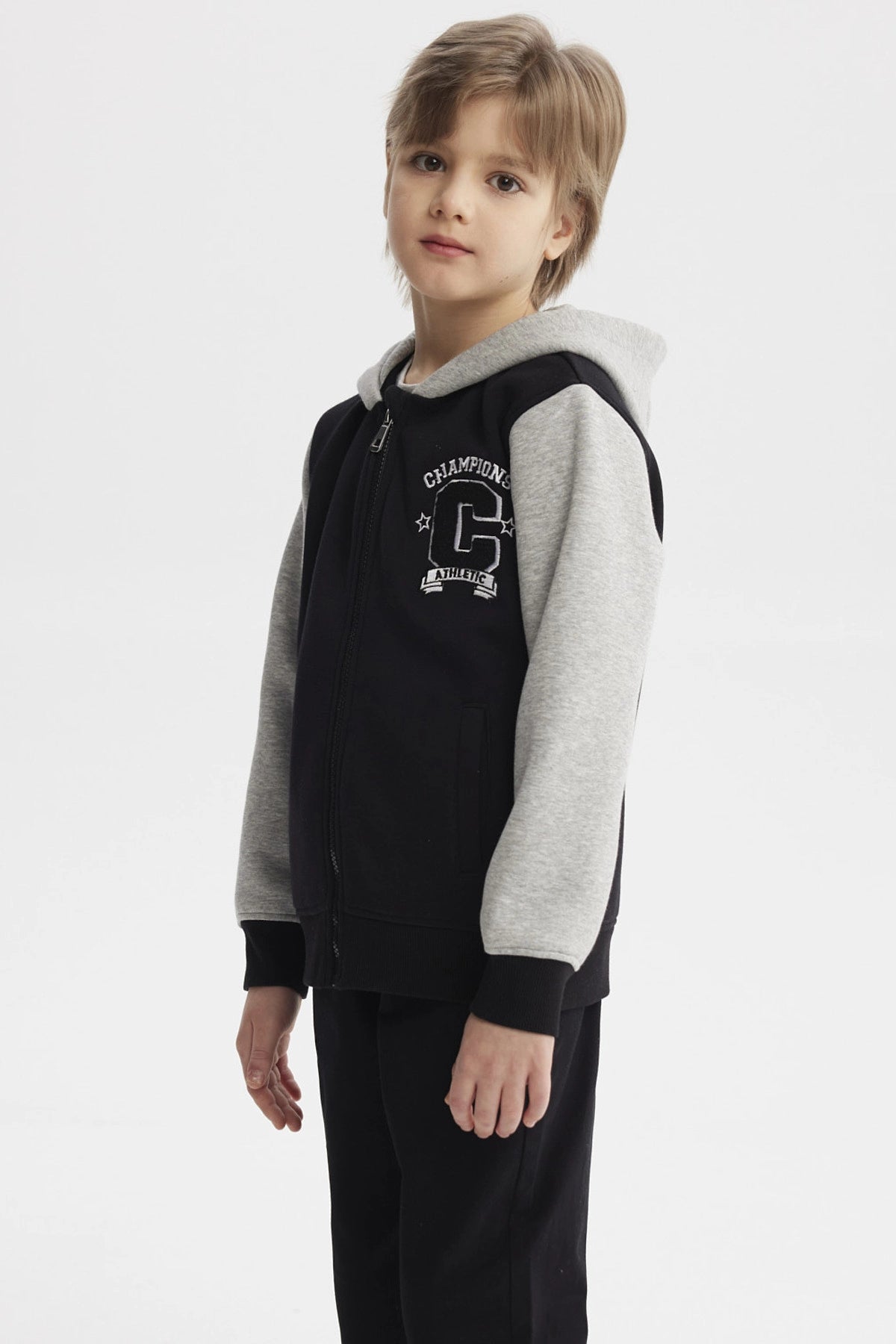 Chaqueta negra para niño con capucha y mangas grises diseño Champion C en el pecho estilo casual urbano