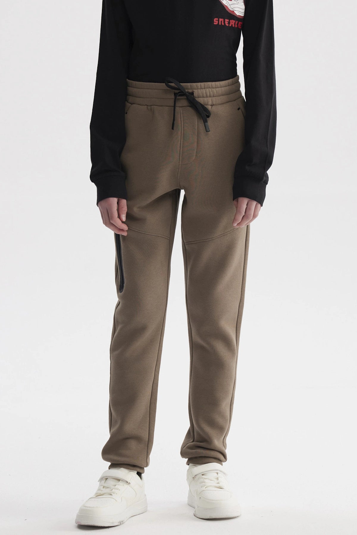 Pantalón buzo niño pitillo café claro con cintura elástica y cordón negro prenda lisa y ajustada