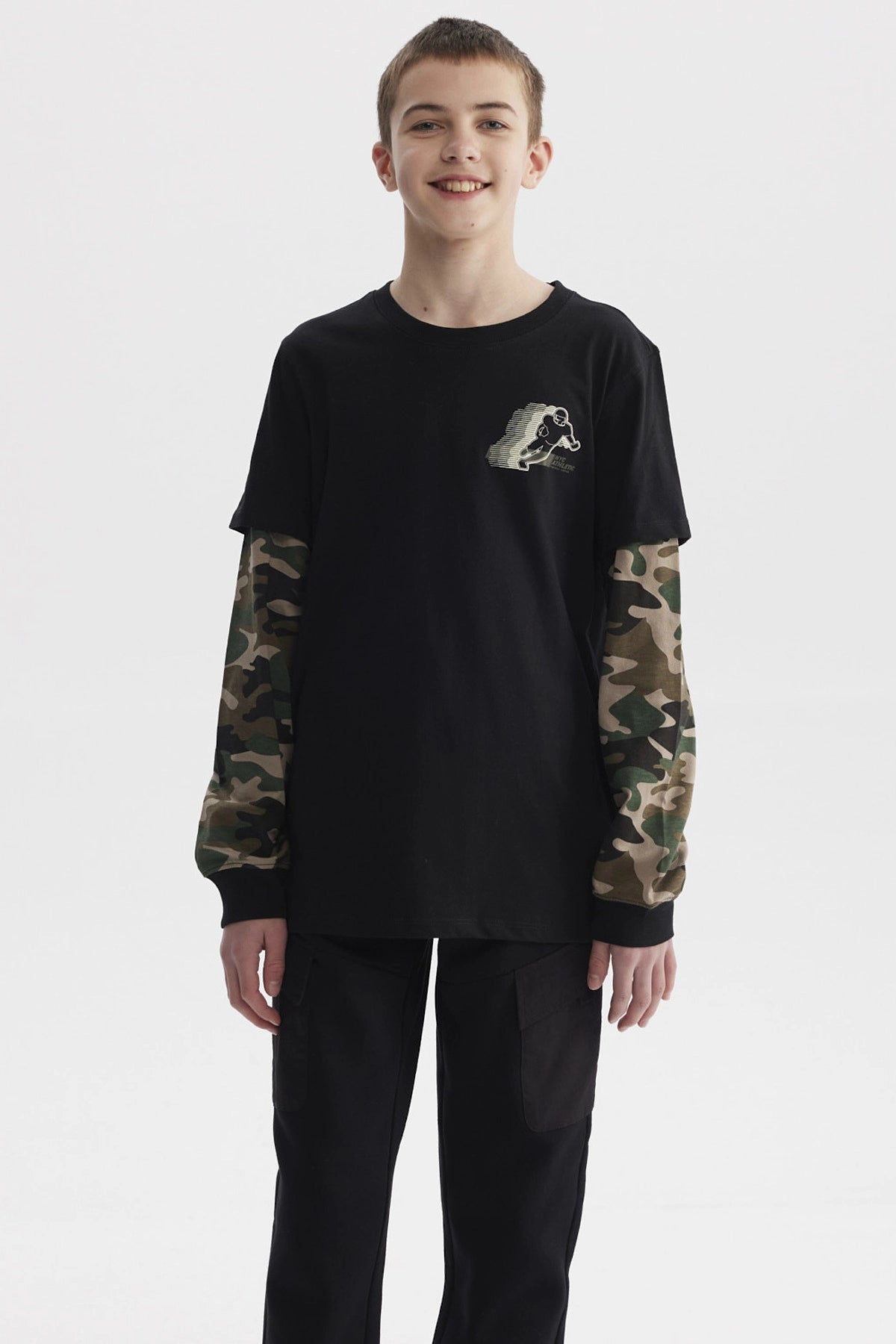 Polera negra de niño con mangas dobles camufladas y estampado de skater pequeño en el pecho estilo gráfico urbano