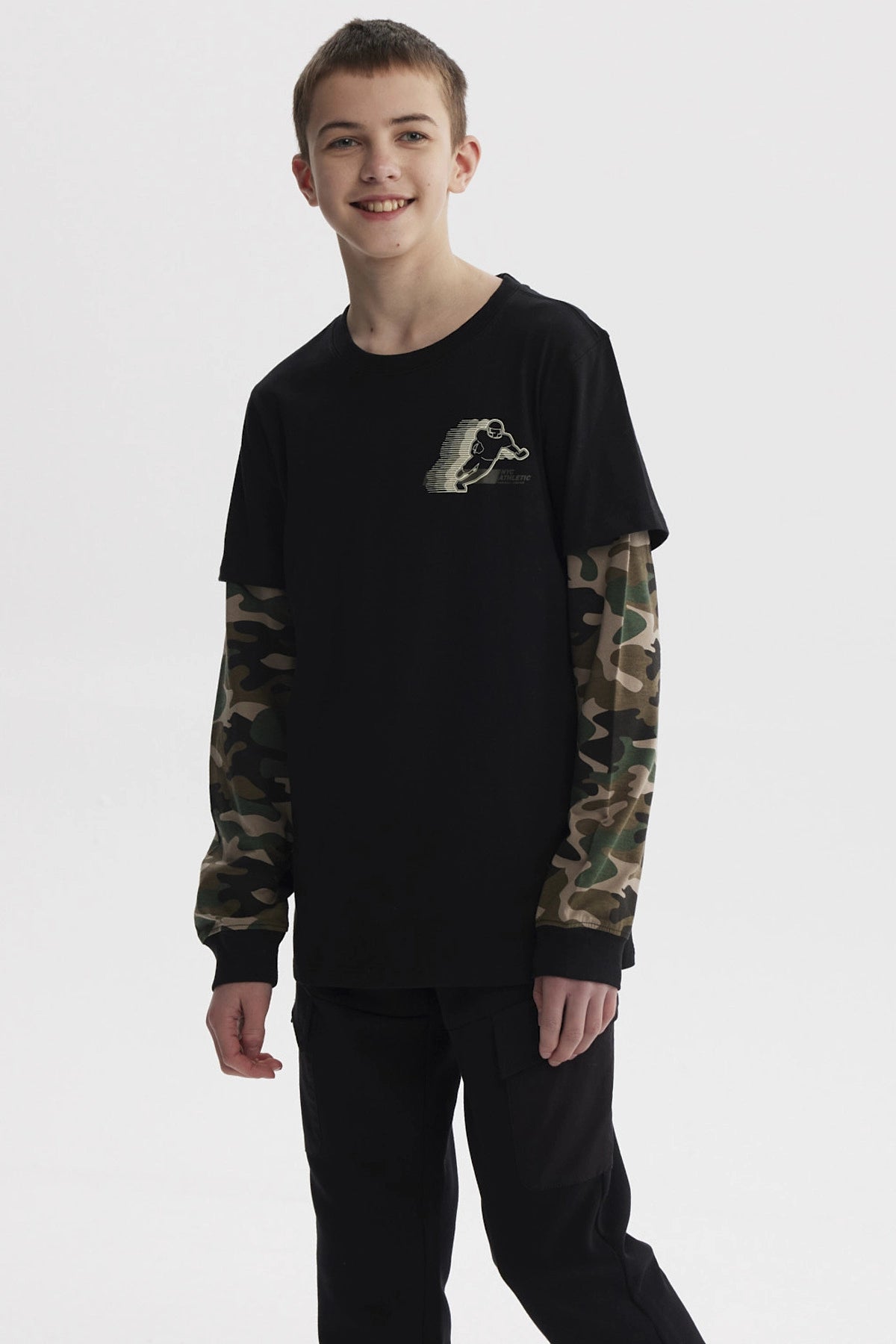 Polera negra de niño con mangas dobles camufladas y estampado de skater pequeño en el pecho estilo gráfico urbano