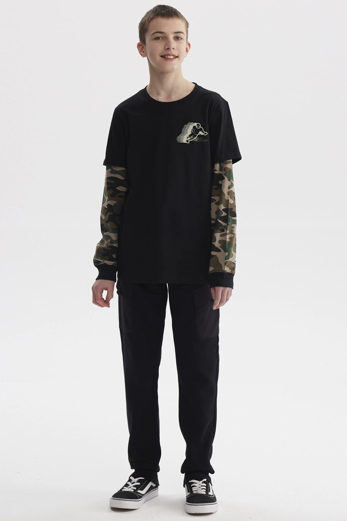Polera negra de niño con mangas dobles camufladas y estampado de skater pequeño en el pecho estilo gráfico urbano