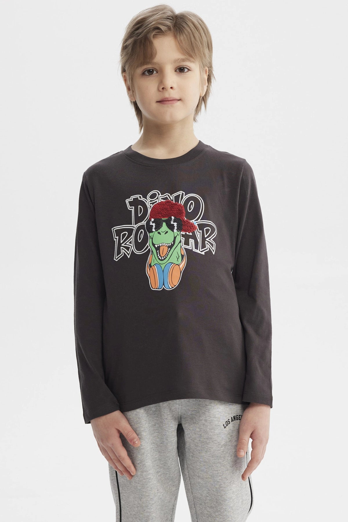 Polera de niño marengo con estampado de dinosaurio rockero con audífonos y gorra roja en el centro estilo dibujo animado