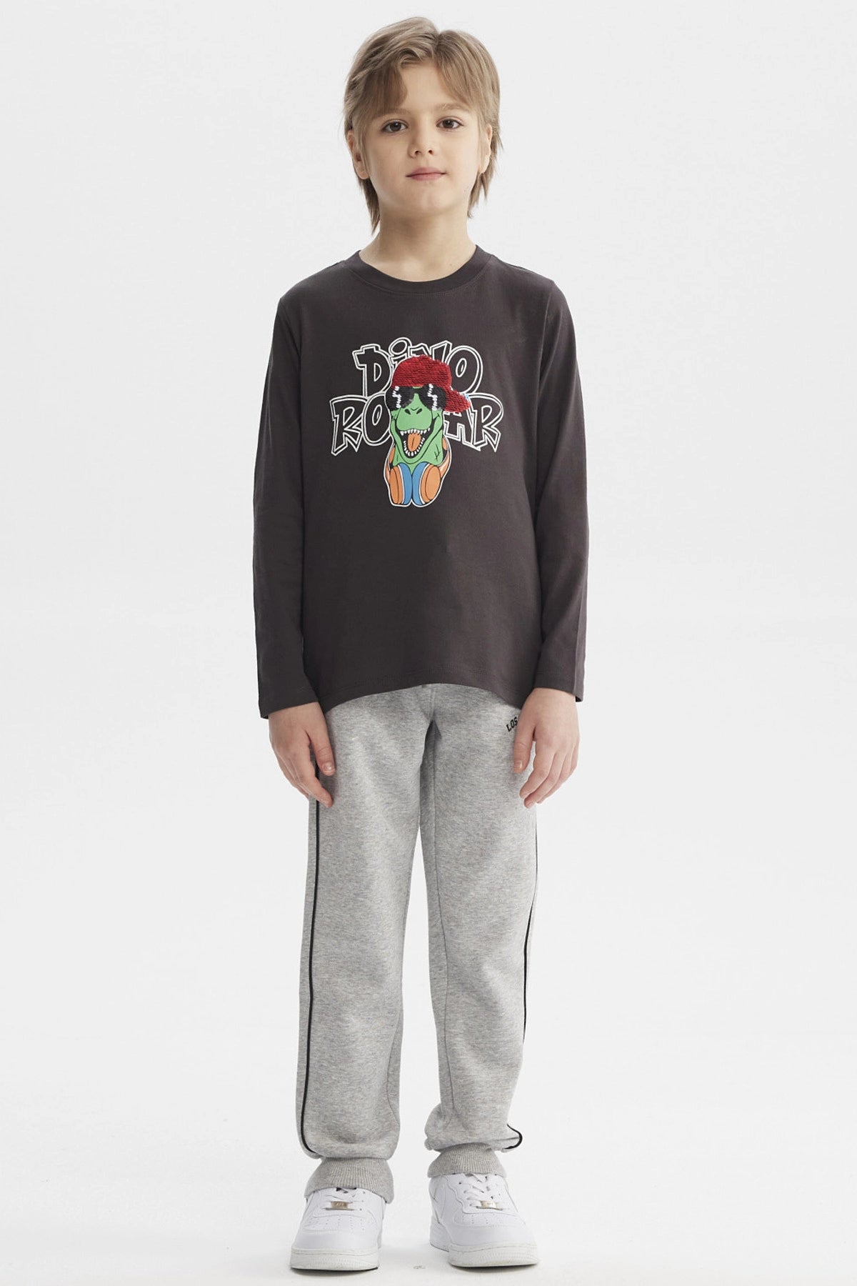 Polera de niño marengo con estampado de dinosaurio rockero con audífonos y gorra roja en el centro estilo dibujo animado