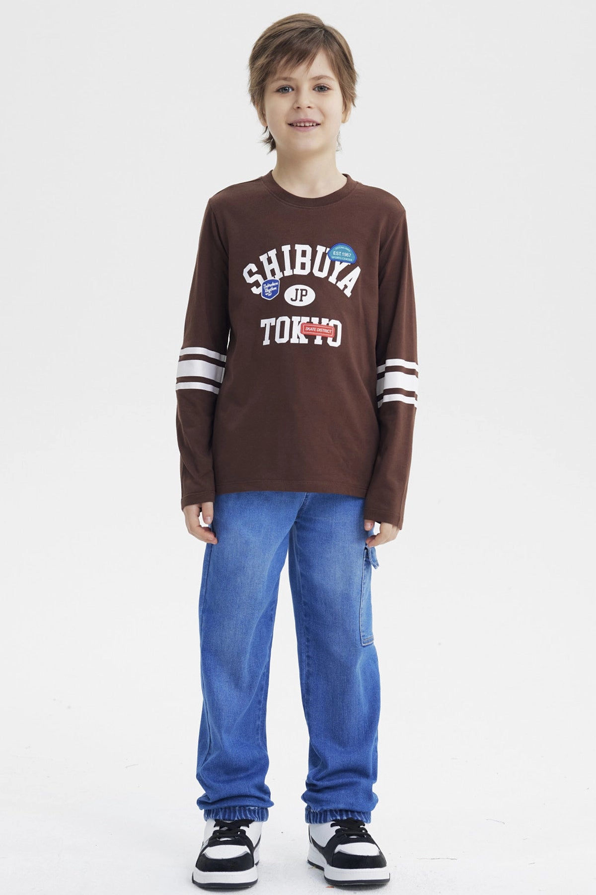 Polera slim café para niño con texto Shibuya Tokyo en el pecho y detalles gráficos urbanos manga larga con rayas blancas