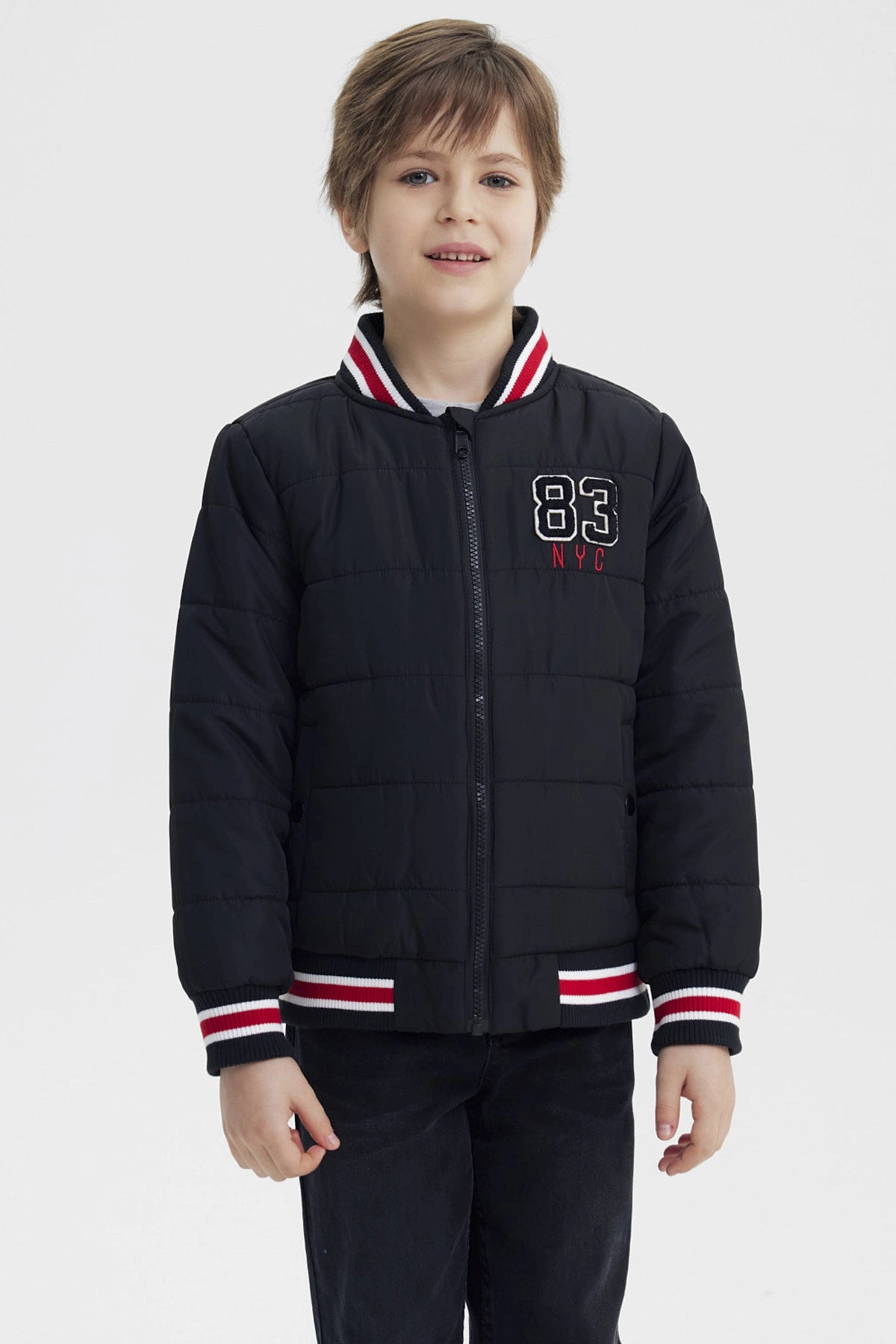 Parka negra para niño con cierre y cuello de rayas rojas y blancas con bordado 83 NYC en el pecho estilo casual