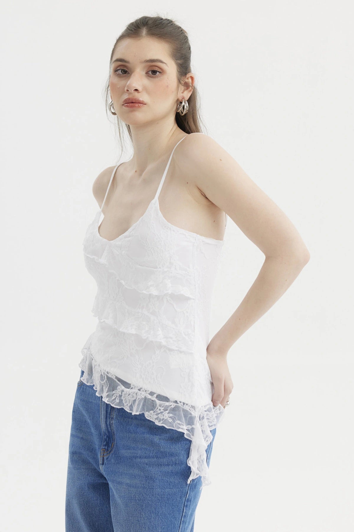 Peto blanco con basta asimétrica y encaje floral sobre fondo liso estilo casual