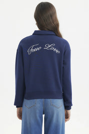 Polerón mujer slim azul con cuello polo y botones delanteros diseño escudo y texto blanco en el pecho estilo casual