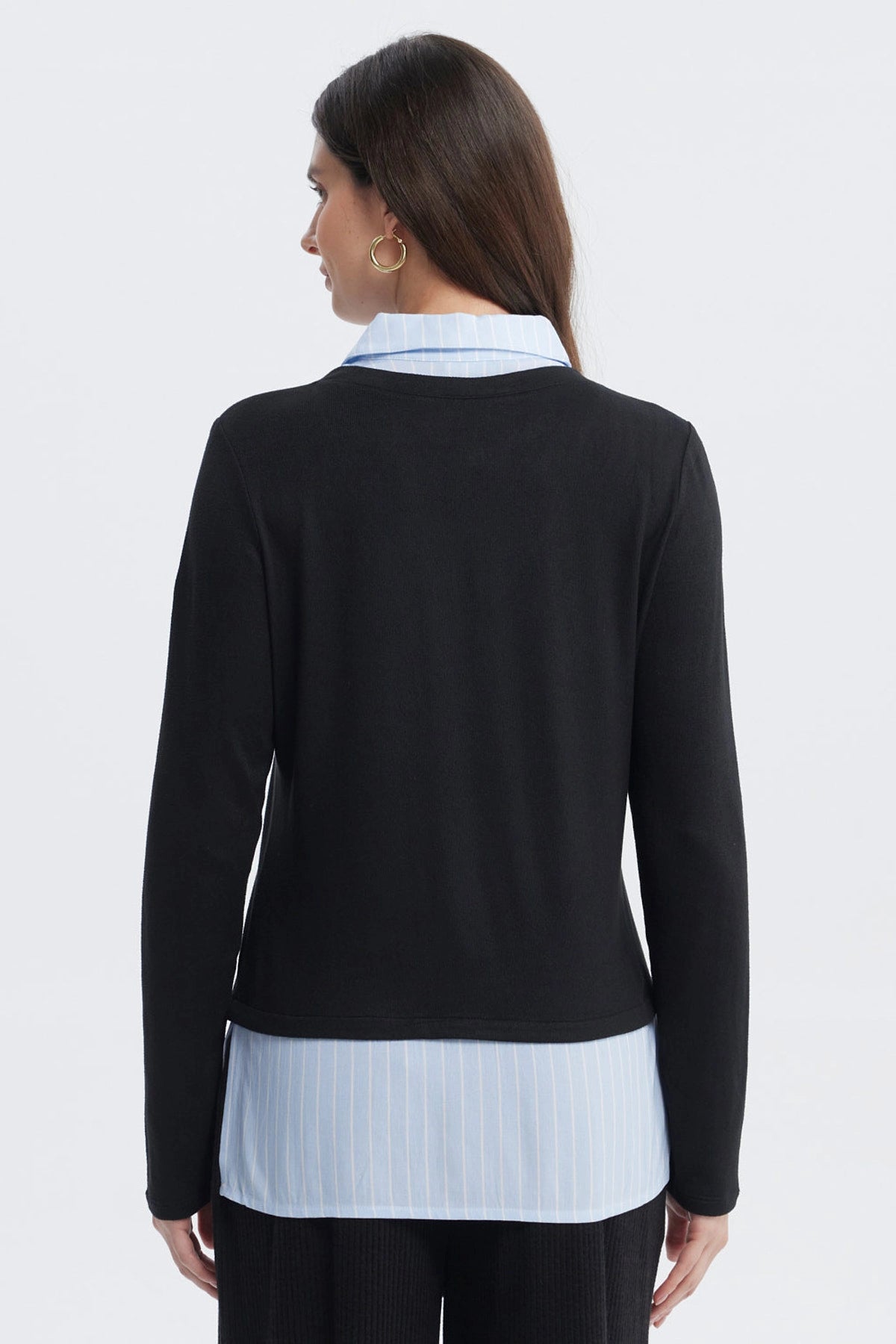 Sweater casual negro de mujer con cuello en V sobre camisa azul con rayas blancas visible en el borde inferior