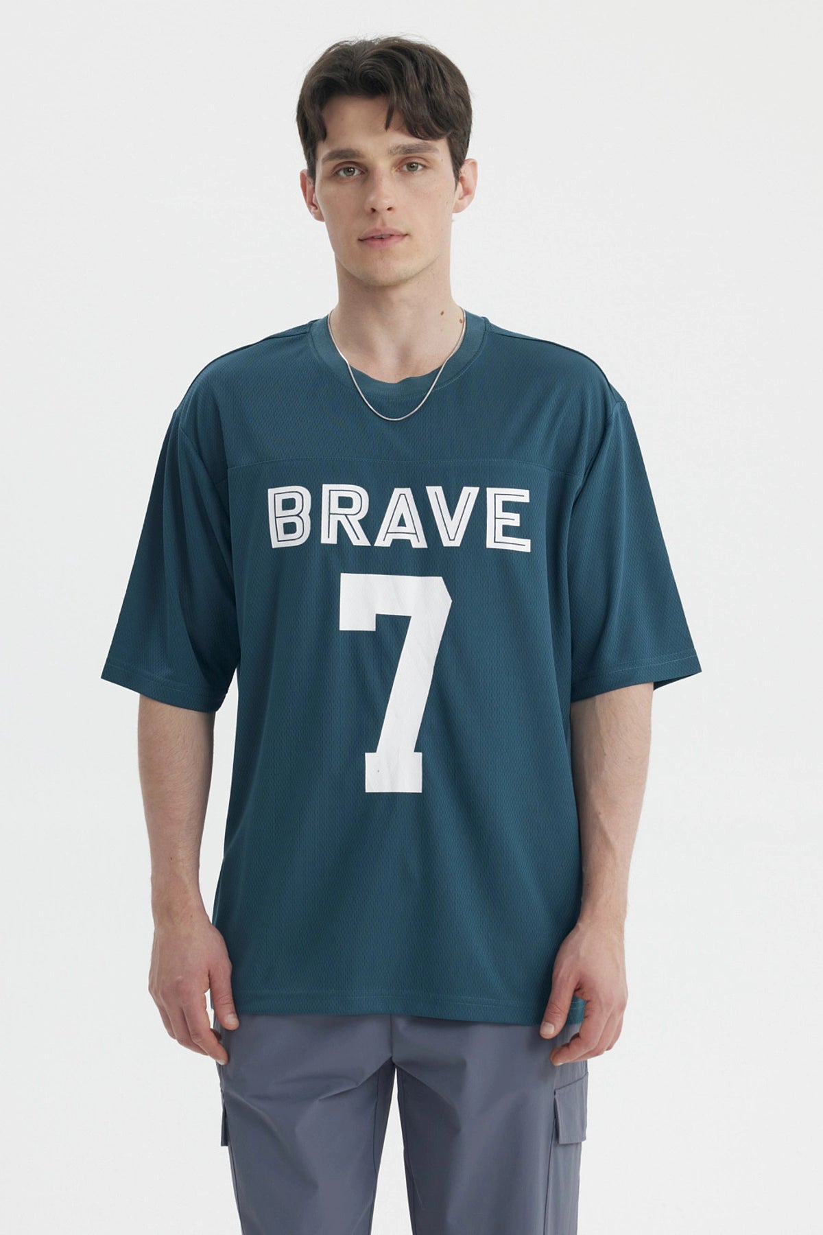 Polera oversize petróleo con texto BRAVE 7 en blanco centrado al frente estilo deportivo y casual
